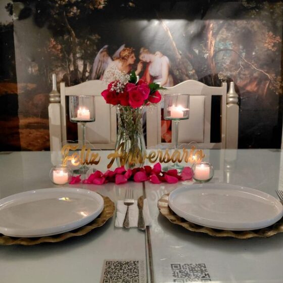 Mesa para dos con centro de rosas, velas y letrero de feliz aniversario