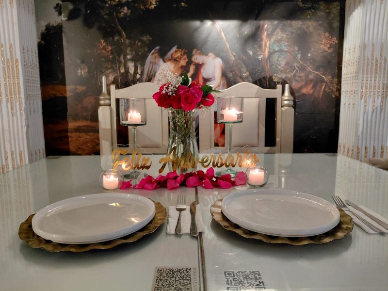 Mesa para dos con centro de rosas, velas y letrero de feliz aniversario