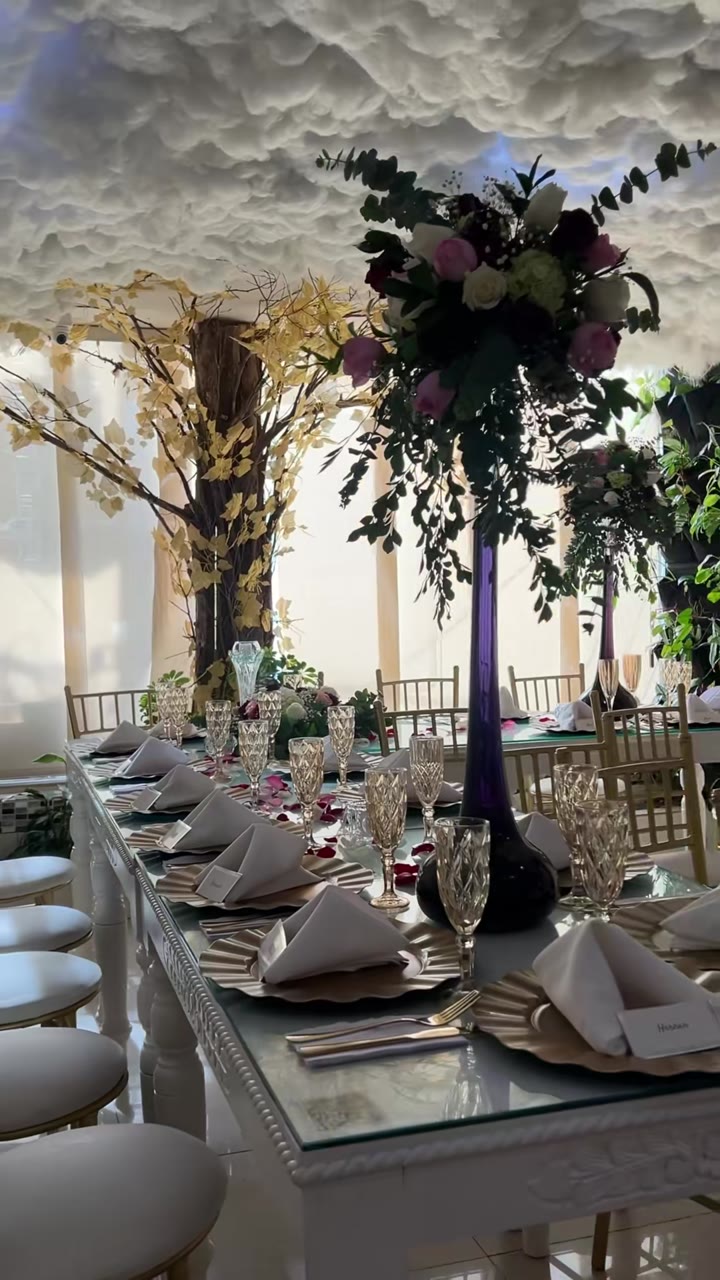Mesa larga para una boda bajo el techo de nubes, con centros de flores altos