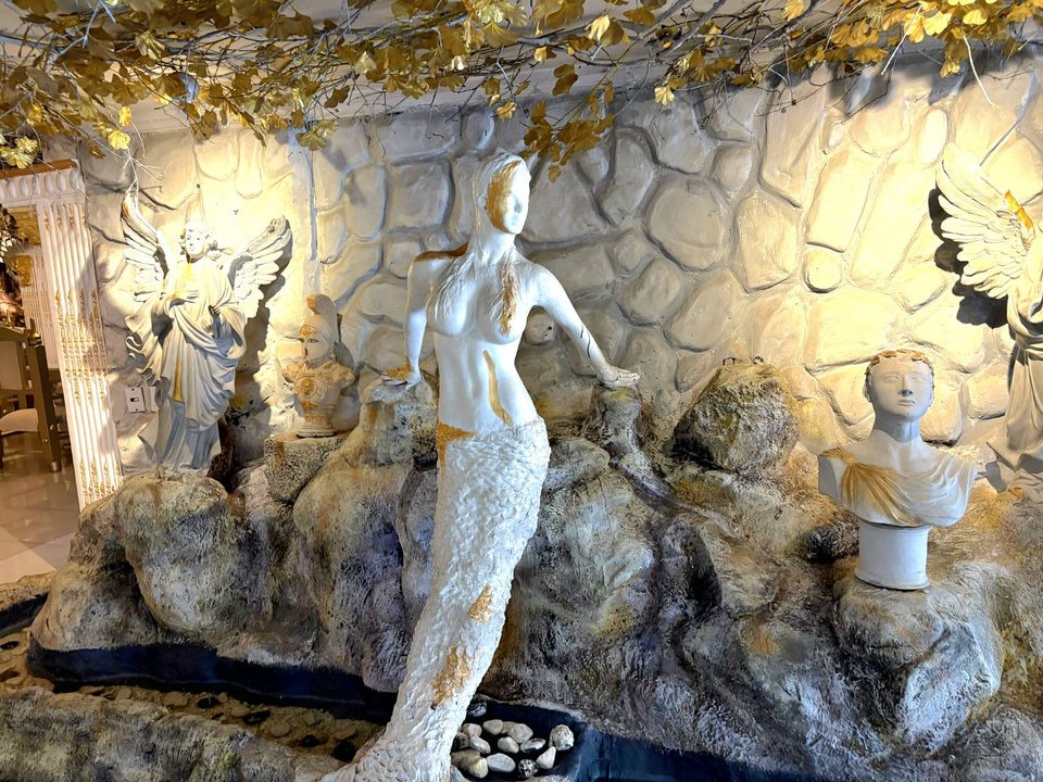 Fuente de piedra con la estatua de una sirena y bustos clásicos en Celestial